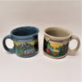 Two mugs with ADIRONDACKS lettered on the top. Mug on the left is turqoise blue with the solid-colored handle on the left side and the front image snow-capped mountains, evergreens, blue tent with a campfire and camper van in the foreground. The mug on the right is off-white with the handle on the right. The image in front is a sunset in the background. Evergreens and water in the mid-section and a red tent, campfire and greenery in the foreground.