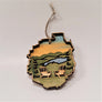 A pair of Adirondack chairs in the Adirondack Park ornament. The chairs are natural wood raised on a green background with a blue stream and golden sky. An evergreen is on the edge next to each chair.