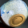 side and bottom view of ceramic bowl green with blue speckle glaze left side and two thirds of bottom right. Blue speckled glaze on top. Bottom unglazed golden.
