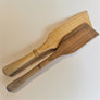 Two spatulas lie flat on a white background. Left top is a light grained spatula with a dark wood spatula below.