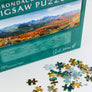 Close up of the bottom of the jigsaw puzzle box with about a dozen loose pieces in front on a white background.