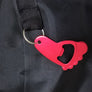 Red metal bottle opener, shaped like a paw, attached to a black strap hanging from the black carrying case.