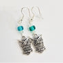 Silver owl earrings lying flat with aqua glass bead and clear bead above the owl on silver hangers.