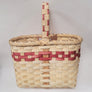 Woven wine basket in neutral color with mauve trim in top third of basket and mixed in with handle above the basket.