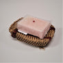 Pack basket soap dish with a bar of pale pink soap in plastic wrap sitting on top.