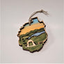 Natural wood camp tent raised on a green background set in the Adirondack Park ornament. Silver blue stream in center surround by green under a golden sky.