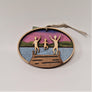 Three natural wooden children figures jumping off a brown wooden dock are featured in the center of this oval ornament. Silver blue water surrounds the dock with green mountains and purple sky in the background.