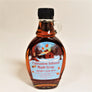 Upright clear syrup bottle with small clear glass handle on the right. Black screw cap on top, Cinnamon Infused Maple Syrup Bechard's Sugar House label on 2/3 of the bottle with the picture of a barn and maple trees with taps on them.