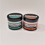 Containers of Hand and Foot Therapy side by side. On the left is a white round container with a black twist top. The labeling is green and black with a gray hand print to the left of the words Hand Therapy. To the right is a white container with a black twist lid and orange and black label. A gray footprint appears to the left of the words Foot Therapy.