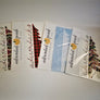 Fanned out display of Adirondack Peach half pine tree decals. Four packets display the pink aztec, buffalo plaid, white and navy floral patterns.