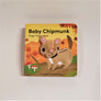 Baby Chipmunk finger puppet book with cloth head of chipmunk coming out of the flat book cover. Chipmunk is beige with black and white stripes and a brown tail. Drawn on a brown path with mushrooms and bushes surrounding.