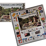 Saranac Lake-Opoly box with bottom right side covered by the open game board. SARANAC LAKE-OPOLY printed in center over a photo of the center of town with all of the participating businesses in town on various property rectangles on the gameboard.