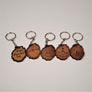 Five brown leather keychains with the shape of the Adirondack Park depicted on each with silver rings attached above each. Within the Park outline from left to right: ENTERING Adirondack Park; SARANAC LAKE NY; 46-R ADIRONDACK set in a mountain outline; 46-R ADIRONDACK set below a mountaintop with a flag planted in the center; 6er SARANAC LAKE set inside a mountain range.