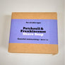 Patchouli and frankincense shave soap flat in its natural wrapping with purple-colored label in center.