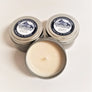 Three candle tins. Two closed 4 ounce candles in the background, one open tin standing head on with wick pointing forward