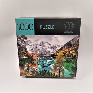 Puzzle box cover with 1000PCS. printed on top alongside the word PUZZLE and an actual-size piece illustration. Below is a full-color photo of the puzzle featuring snow-covered mountains reflected in a pool of water below in between mountains with autumn colors and greenery.