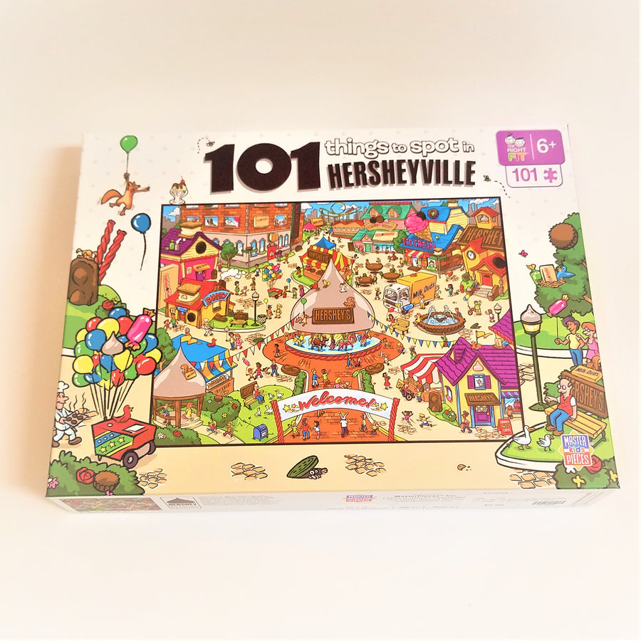 Puzzle box cover for 101 things to spot  in Hersheyville featuring the amusement park. Colorful balloons and street scene  surround the square  outside the park.