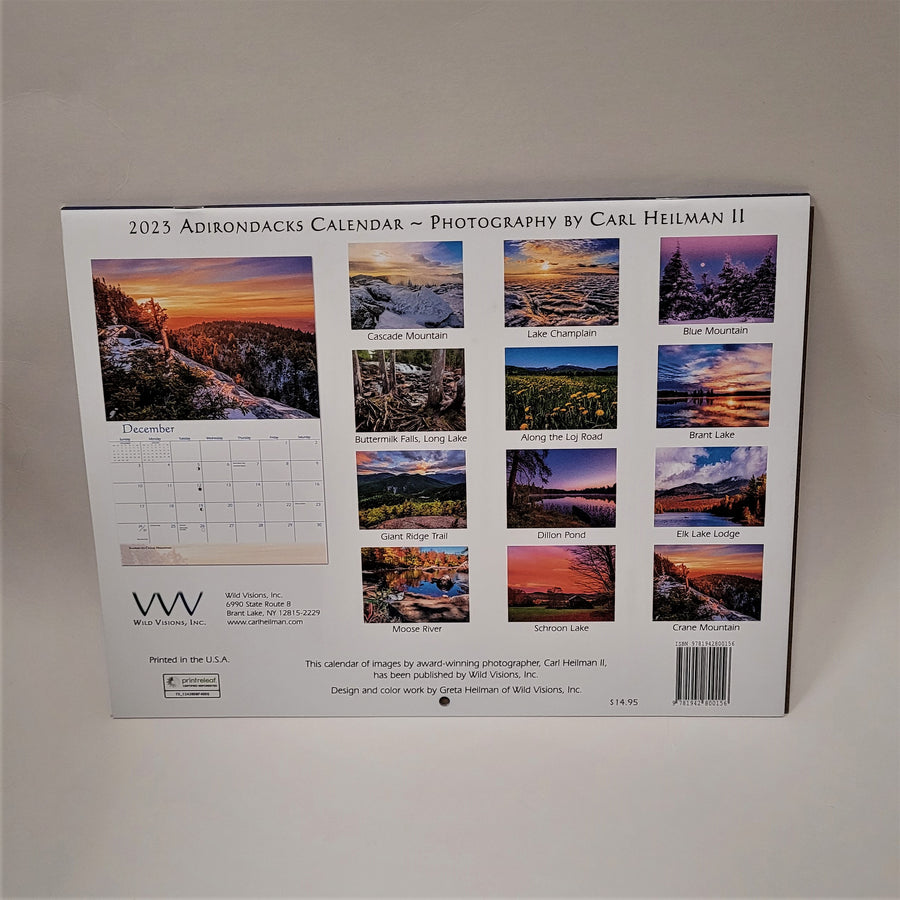 Back cover of the 2023 Carl Heilman Adirondacks Calendar. On the right side all 12 scenes from the inside are depicted in full-color miniature photos labeled with the name of the view. On the left side the calendar is open to display the December photograph above the calendar grid of days and dates.