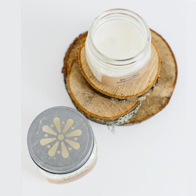 From left to right, looking down at candle and jar, silver lid with daisy design; open candle jar sitting on birch bark