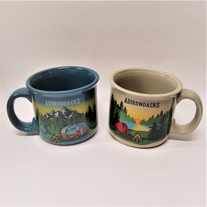 Two mugs with ADIRONDACKS lettered on the top. Mug on the left is turqoise blue with the solid-colored handle on the left side and the front image snow-capped mountains, evergreens, blue tent with a campfire and camper van in the foreground. The mug on the right is off-white with the handle on the right. The image in front is a sunset in the background. Evergreens and water in the mid-section and a red tent, campfire and greenery in the foreground.