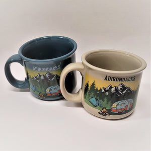Two mugs with both handles on the left side. Both mugs have the same center image: snow-capped mountains, blue tent, campfire and camper van. The turquoise-blue mug on the left has the word ADIRONDACKS in white above the image. The off-white mug on the right has the word ADIRONDACKS in a dark color (either black or dark green) printed above the image.