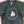 Green t shirt hanging with short sleeves folded in. White Eagle Island logo of 3 trees, inside a white semi-circle with white Eagle Island Camp lettering below.