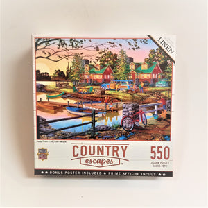 Cover of puzzle box features bucolic scene with two cottages and period station wagons behind a dock area with canoes and boats. A rustic lane is to the right with a fence and bicycle. People are waving from the dock  while other people are unloading a car and one person leans on the fence with a dog beside him. Bottom o f box has title type and name of company 550 puzzle.