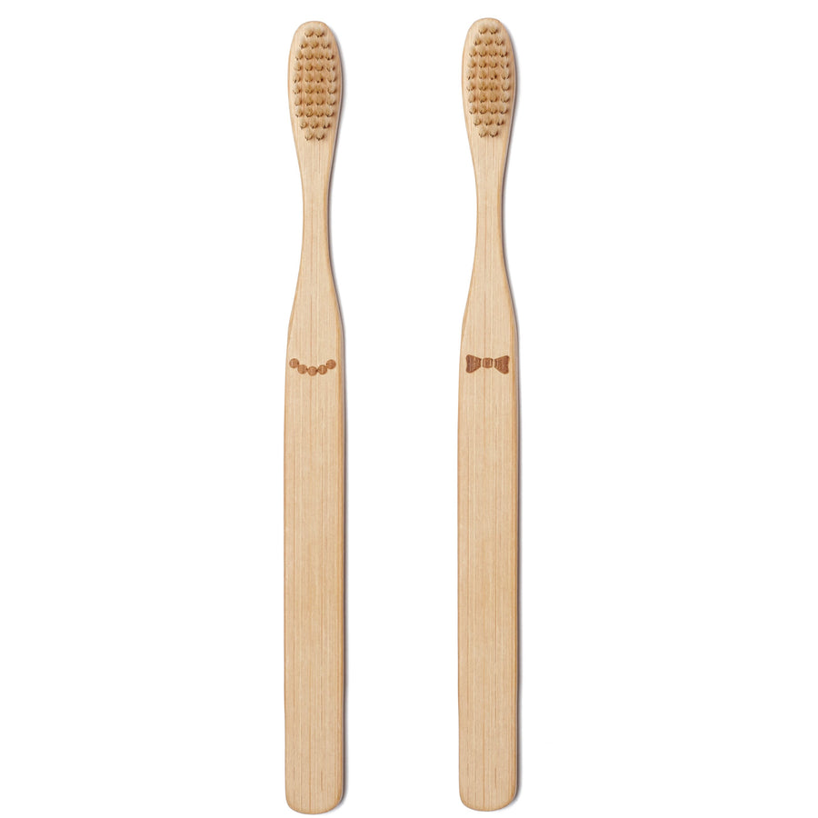 Two bamboo toothbrushes side by side; Hers on the left with five brown beads centered below the bristle top; His on the right with a brown bow tie centered below the bristle top.