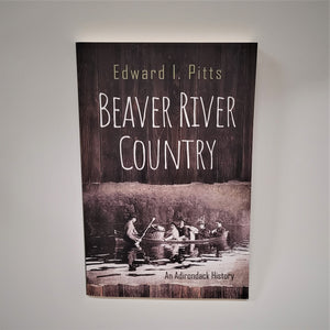 Cover of Beaver River Country book.  Lower half pictures 5 travelers with a large pack basket in a very full canoe. The words An Adirondack History are printed on the bottom right with the title and author printed above the canoe scene on  what appears to be a wooden panel. BEAVER RIVER COUNTRY in white below Edward I. Pitts in safe green.