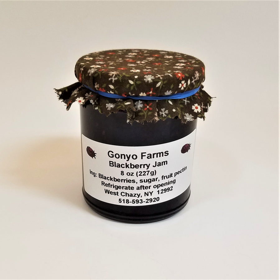 Brown cloth cover with orange and beige flowered pattern banded to a jar of Gonyo Farms Blackberry Jam.