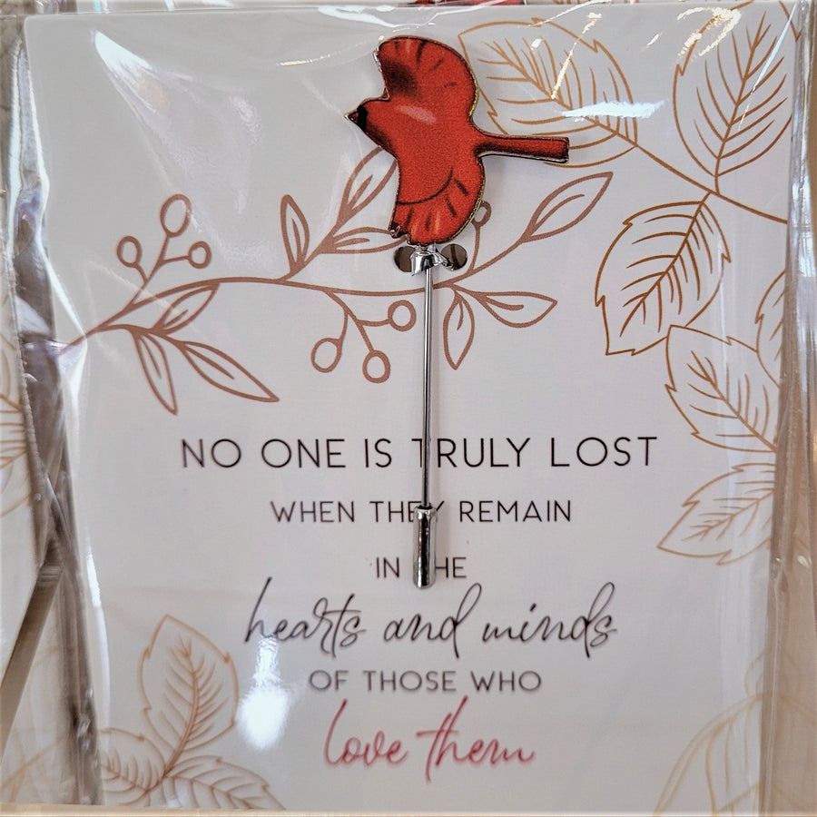 Single Cardinal pin with bird with wings spread open in flight front on an illustrated card with the words NO ONE IS TRULY LOST WHEN THEY REMAIN IN THE HEARTS AND MINDS OF THOSE WHO LOVE THEM printed in bottom center. All seen through plastic packaging.
