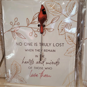Single Cardinal pin with bird upright facing front on  an illustrated card with the words NO ONE IS TRULY LOST WHEN THEY REMAIN IN THE HEARTS AND MINDS OF THOSE WHO LOVE THEM printed in bottom center. All seen through plastic packaging.