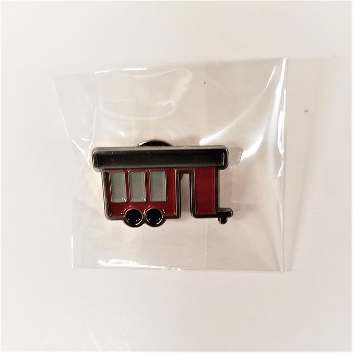 Inside clear packaging is the pin of the Cure Porch on Wheels with a black top, 3 gray vertical windows set in the maroon conveyance with two black wheels on the bottom left and a small rectangular opening for the door
