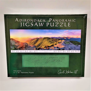 Box cover of Adirondack Panoramic Jigsaw Puzzle features a dark green border white type a four-color horizontal photo of sunlight mountain range and a lighter green horizontal inset diagram mountain reference chart.