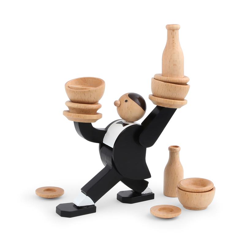 Wooden waiter dressed in painted black-and-white tux-like attire holding up small wooden bowls dishes and decanters. At his feet are more wooden dishes, bowls and a decanter.