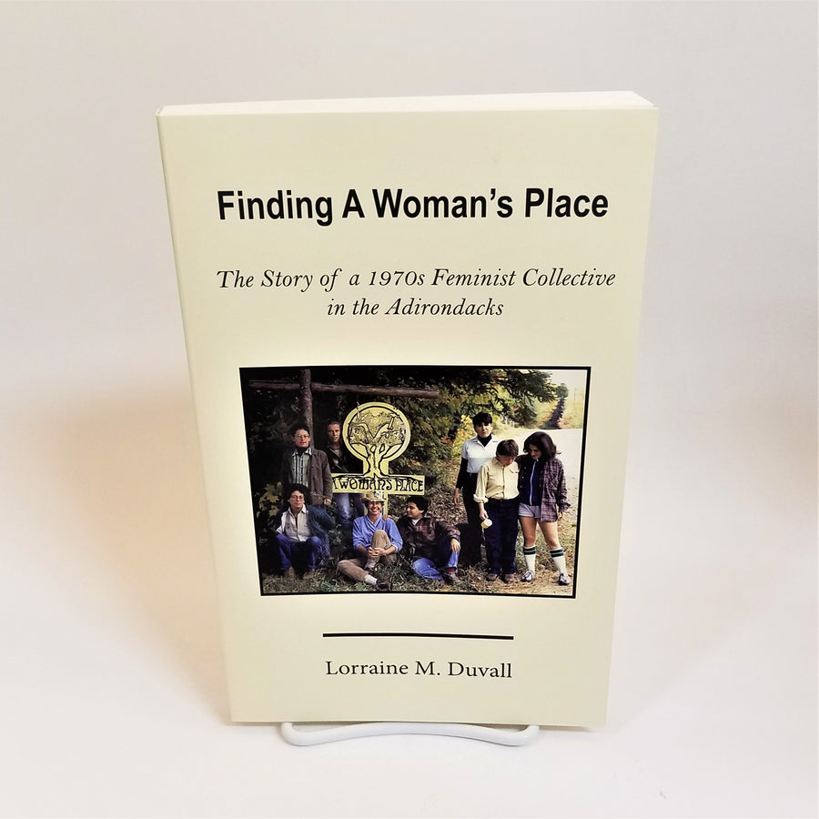 Book Finding a Woman's Place displayed standing up. Cream-colored cover with photo of people in center around Woman's Place logo.