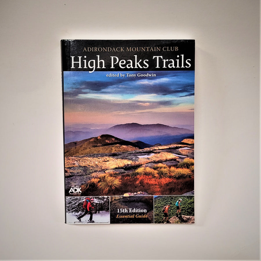 Cover of the book High Peaks Trails features full-color photographs. The largest in the center of the cover is of the high peaks with various shades of blue sky and purple and gold mountains. Below on either side of type that says: 15th Edition, are two photos. The one on the left is of a cross-country skier and to the right are two hikers.