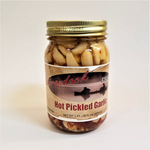 Glass jar of Hot Pickled Garlic with lots of peeled garlic cloves and specs of red and seeds showing through the jar around the label under the gold screw top.