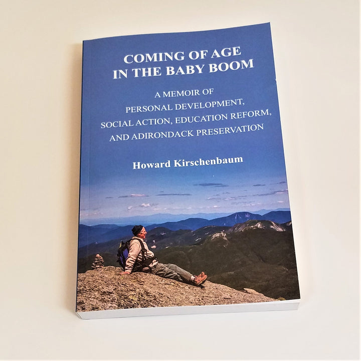 Cover of book Coming of Age in the Baby Boom with lots of blue sky over Adirondack mountains. In the foreground a person rests on top of a mountain peak enjoying the view.