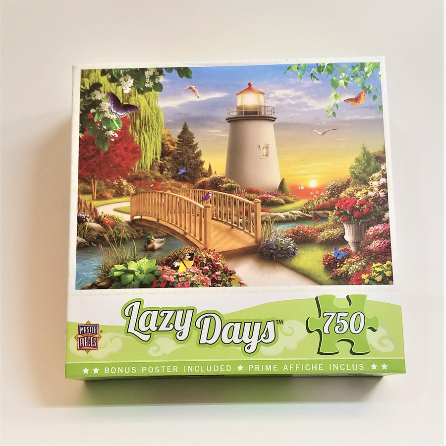 Lazy Days 750 piece jigsaw puzzle box cover. Features a square photo of a light house at sunrise. In the foreground is a wooden arched bridge over a stream with lots of colorful flowers on a green lawn and grown trees in the left background.