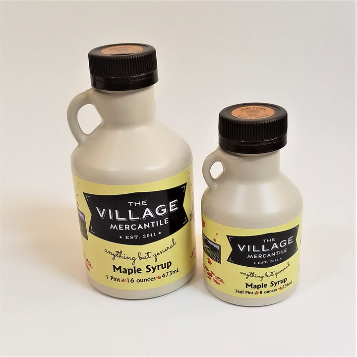 Two different sizes of maple syrup jugs. Solid jug with handle on the left, black screw top and The Village Mercantile label bottom, mid-section of each.