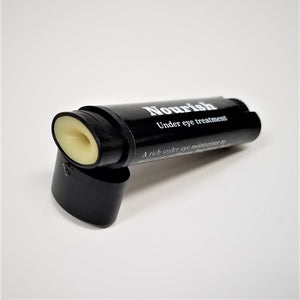 Black cylinder of Nourish--under eye treatment open with the natural color eye stick showing at the end of the container which is resting on the black cap. White text on the black wrap-around label.
