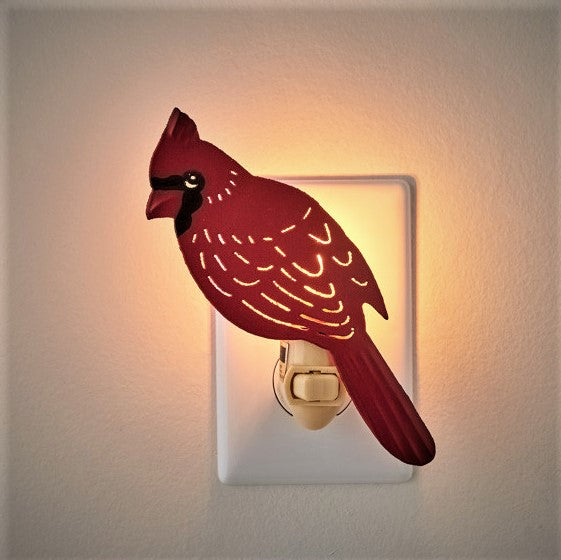 Red cardinal bird night light plugged into socket and turned on so you can see the light shining through the feathers of the bird and around the board.