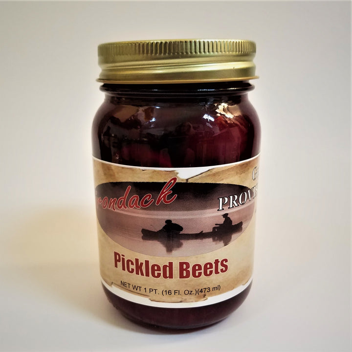 Glass jar of Pickled Beets. Seen through the clear glass is a deep maroon above and below the label under the gold screw top.