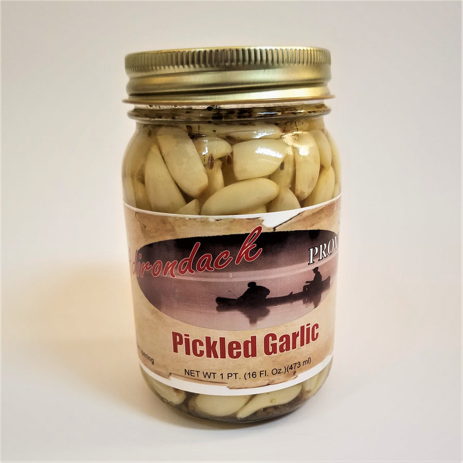 Glass jar of Pickled Garlic with lots of peeled garlic cloves showing through the jar around the label under the gold screw top.