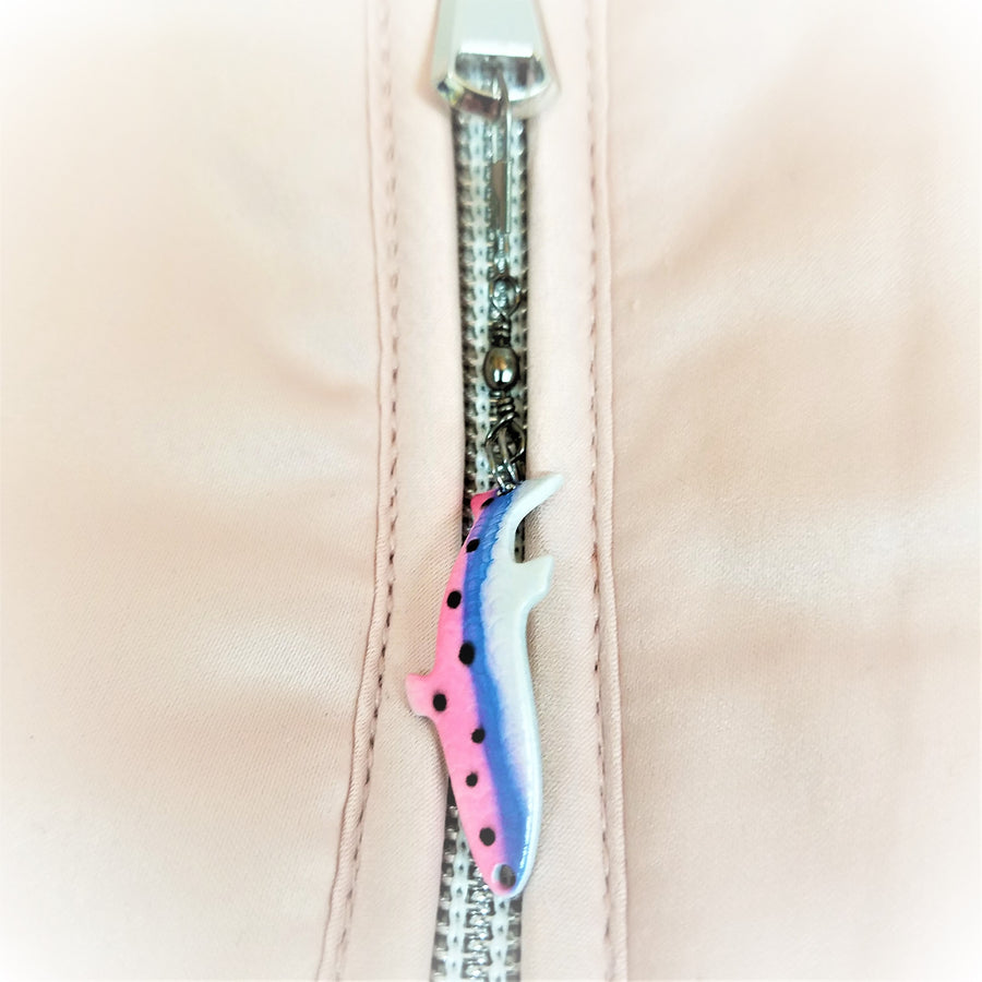 Fish lure zipper pull attached to zipper. Fish points down and is pink, blue and white with black dots on the left in the pink and blue sections.
