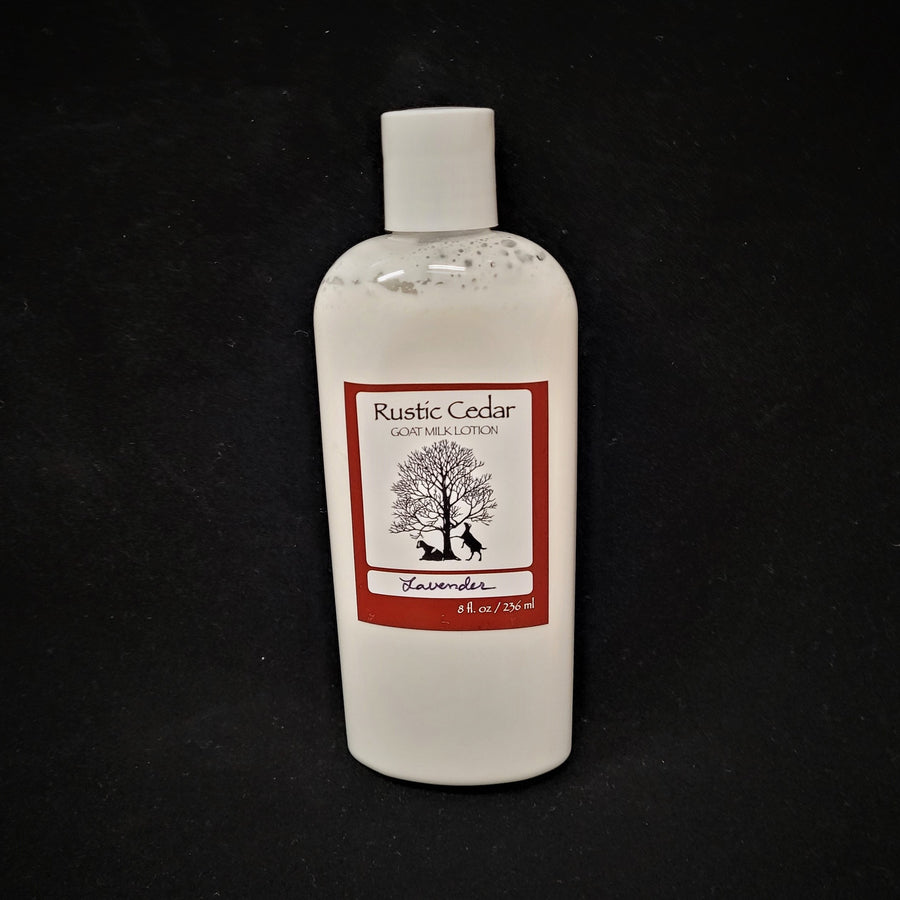 Single bottle of Rustic Cedar Goat Milk Lotion standing straight up. White liquid can be seen through clear plastic around the rectangular label in the center. The label has a rust-colored border with the black tree and goat logo in the center. Above the logo is the text Rustic Cedar Goat Milk Lotion and below in script Lavender with 8 fl.oz. /236 ml below that.