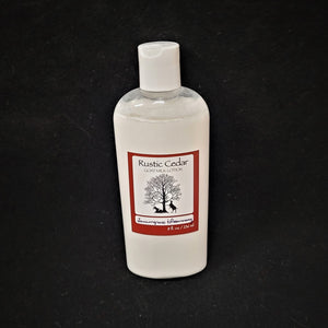 Single bottle of Rustic Cedar Goat Milk Lotion standing straight up. White liquid can be seen through clear plastic around the rectangular label in the center. The label has a rust-colored border with the black tree and goat logo in the center. Above the logo is the text Rustic Cedar Goat Milk Lotion and below in script Lemongrass & Rosemary with 8 fl.oz. /236 ml below that.
