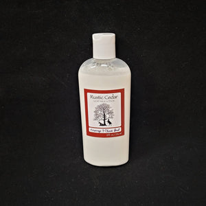 Single bottle of Rustic Cedar Goat Milk Lotion standing straight up. White liquid can be seen through clear plastic around the rectangular label in the center. The label has a rust-colored border with the black tree and goat logo in the center. Above the logo is the text Rustic Cedar Goat Milk Lotion and below in script Orange & Clove Bud with 8 fl.oz. /236 ml below that.