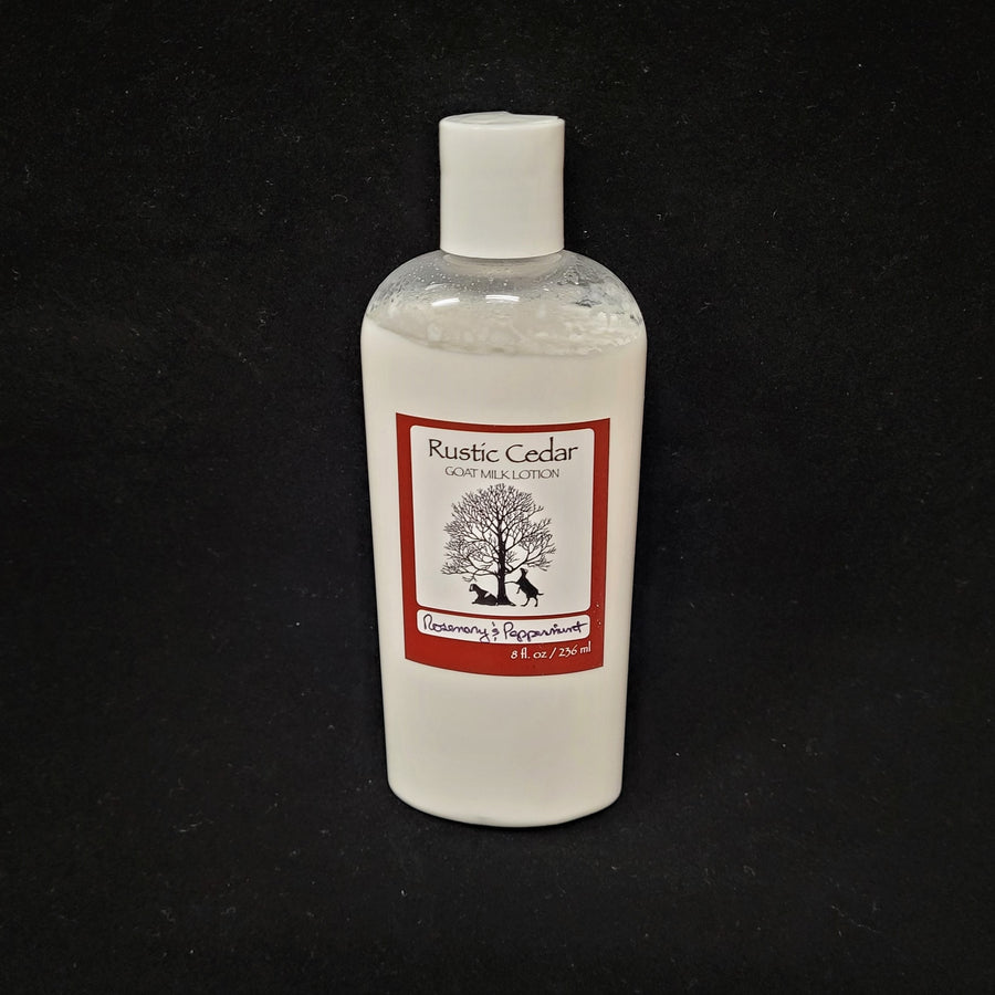 Single bottle of Rustic Cedar Goat Milk Lotion standing straight up. White liquid can be seen through clear plastic around the rectangular label in the center. The label has a rust-colored border with the black tree and goat logo in the center. Above the logo is the text Rustic Cedar Goat Milk Lotion and below in script Rosemary & Peppermint with 8 fl.oz. /236 ml below that.